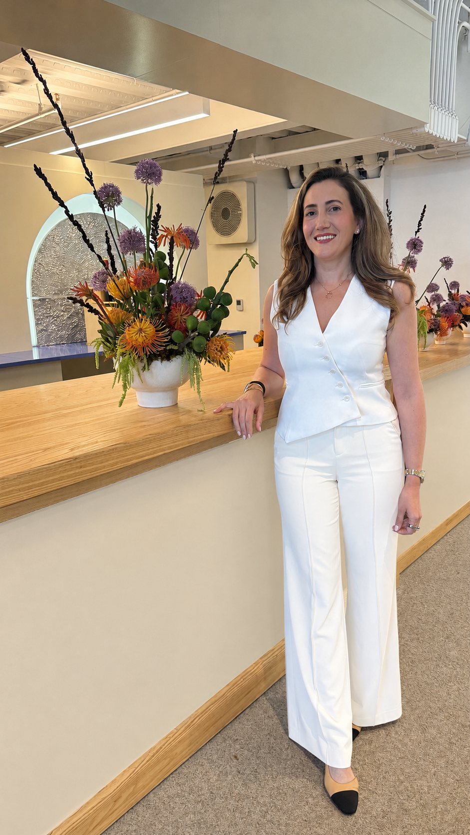 Yasaman Nazhand standing beside a counter of fresh flowers, warm and welcoming