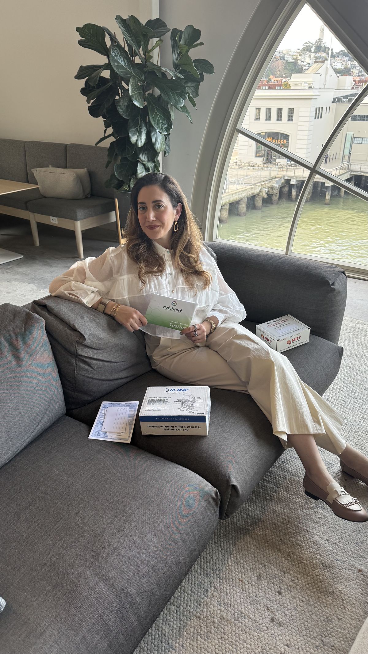 Yasaman seated warmly on the couch with at-home hormone and gut test kits